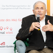 Mark Olsky, mit grauen Haaren im dunklen Sakko, sitzt auf einem Ledersessel und beantwortet Fragen der anwesenden Teilnehmer:innen.