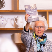Eva Clarke hält das Buch "Schicksalskinder – Die KZ-Babys von Mauthausen" in die Höhe.