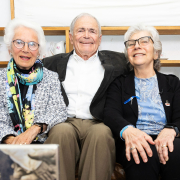 Eva Clarke, Mark Olsky und Hana Berger Moran sitzen auf einem Ledersofa und lächeln in die Kamera.