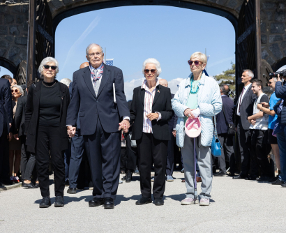 Hana Berger Moran, Mark Olsky, Eva Clarke sowie Katja Sturm-Schnabl gehen Hand in Hand durch das Tor des ehemaligen Konzentrationslagers Mauthausen.
